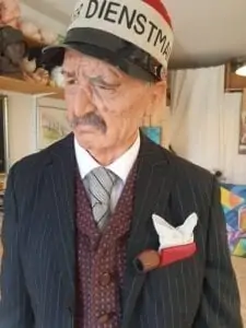 Le persone sono sedute in una stanza poco illuminata e indossano cuffie per la realtà virtuale. Una grande sfera luminosa al centro mostra una scena di persone che ballano in abito da sera. Le pareti sono adornate con ritratti incorniciati e decorazioni ornamentali.