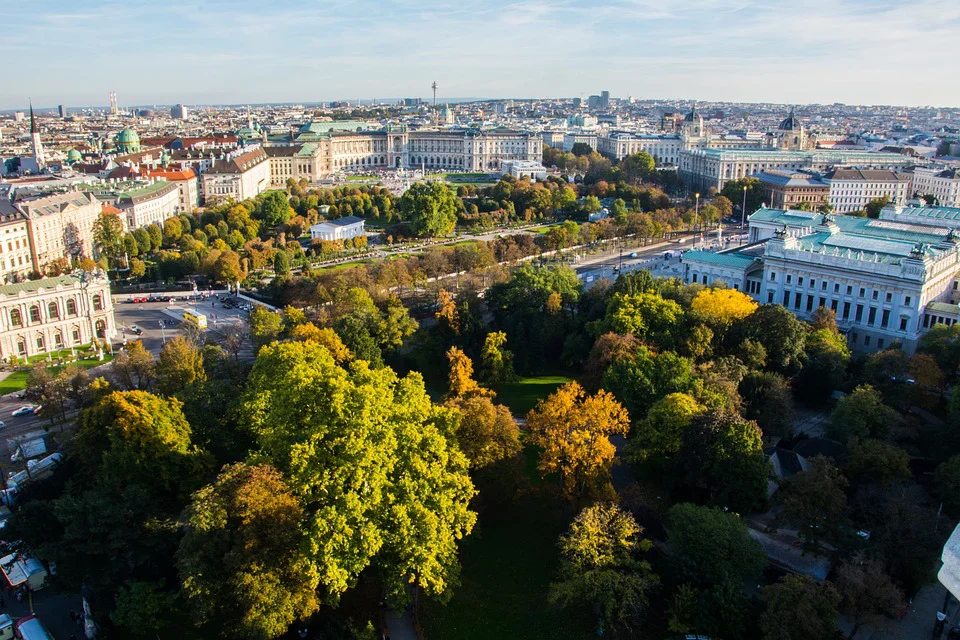 Luftaufnahme einer Stadt mit historischen Gebäuden, von Bäumen gesäumten Alleen und grünen Parkanlagen unter klarem Himmel, die eine Mischung aus Stadt- und Naturlandschaft zeigen.