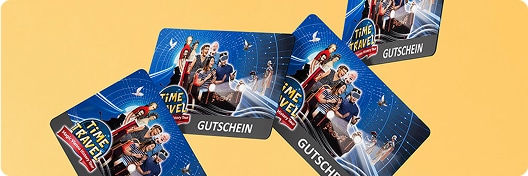 Vier Geschenkkarten zum Thema „Zeitreise“ mit illustrierten Figuren in futuristischer Kleidung auf blauem und schwarzem Hintergrund. Auf jeder Karte ist der Schriftzug „GUTSCHEIN“ aufgedruckt. Die Karten sind auf gelbem Untergrund angeordnet.