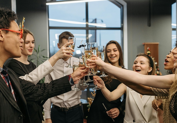 Eine Gruppe von formell gekleideten Personen steht in einem Kreis, lächelt und erhebt Gläser mit Champagner, um in einem modernen Raum einen Toast auszubringen.