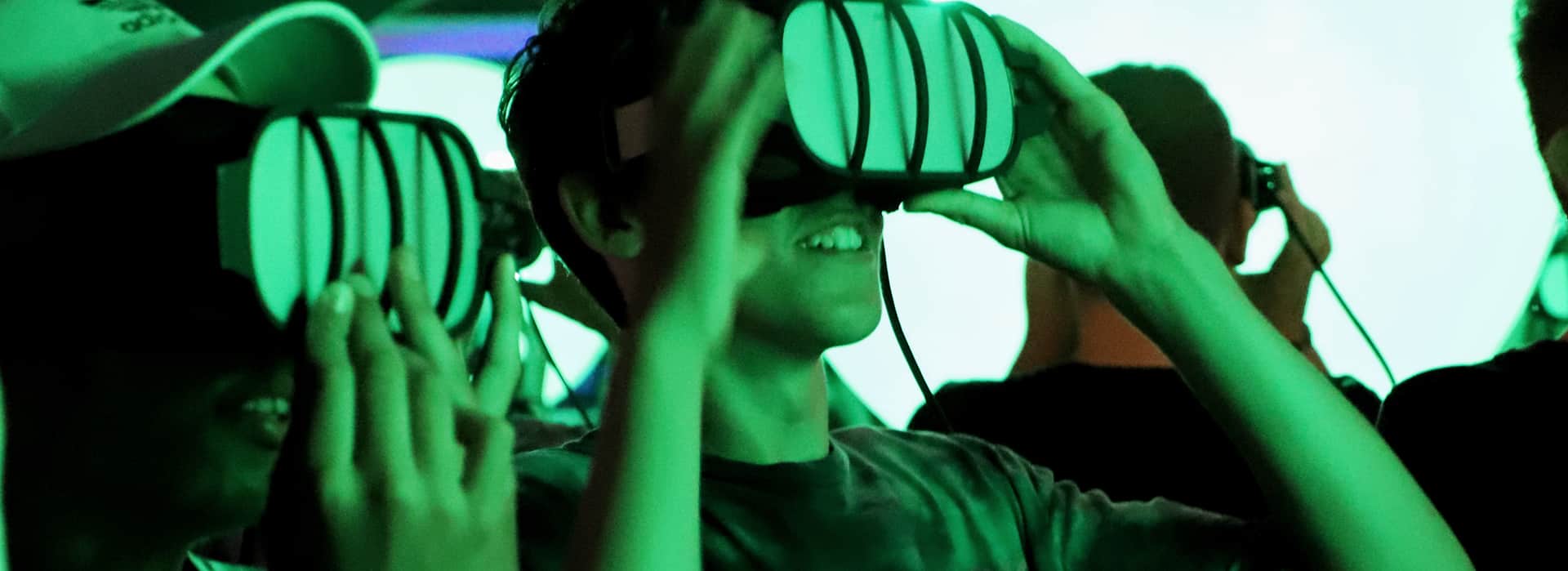 Eine Gruppe von Menschen, die Virtual-Reality-Headsets tragen, l&auml;cheln und in einer hell erleuchteten, gr&uuml;n get&ouml;nten Umgebung interagieren.