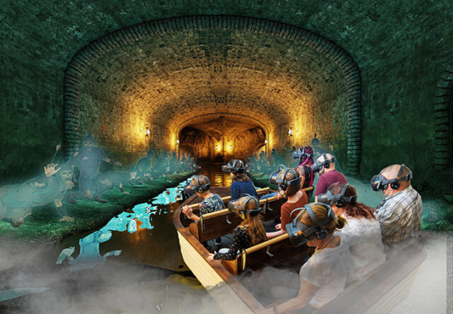Eine Gruppe von Menschen, die VR-Brillen tragen, fährt mit einem Boot durch einen gewölbten, schwach beleuchteten Tunnel, wobei gespenstische blaue Gestalten und Nebeleffekte an den Tunnelwänden und auf dem Wasser erscheinen.