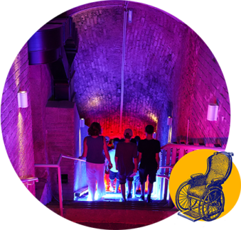 Un gruppo di persone scende una rampa di scale in un tunnel illuminato di viola. In un angolo compare l’immagine di una sedia a rotelle su sfondo giallo, a indicare una scarsa accessibilità.