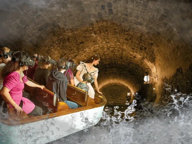 Menschen mit VR-Brillen fahren mit einem Boot durch einen gewölbten Steintunnel, während eine Frau in historischer Kleidung zum Wasser hinblickt.