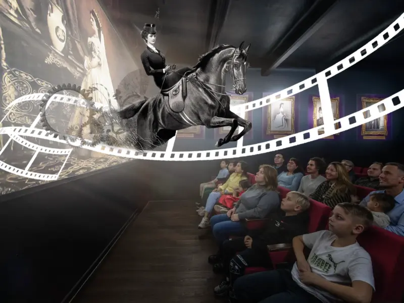 In einem dunklen Kinosaal betrachtet das Publikum eine 3D-Projektion einer Frau in viktorianischer Kleidung, die auf einem Pferd reitet, eingerahmt von einem Filmstreifen.
